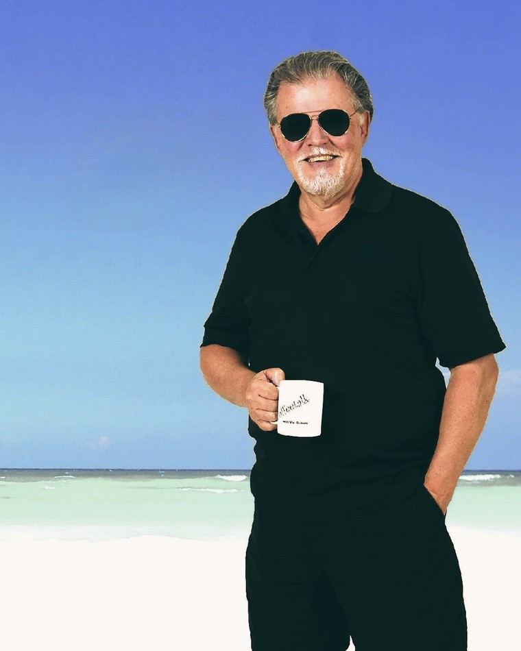 Vic Dubois on the beach, sunglasses on, holding a Sock Hop Radio mug.